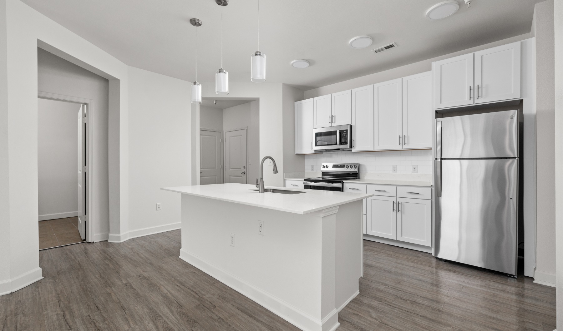 Kitchen with island, stainless steel appliances, wood flooring, and quartz countertops